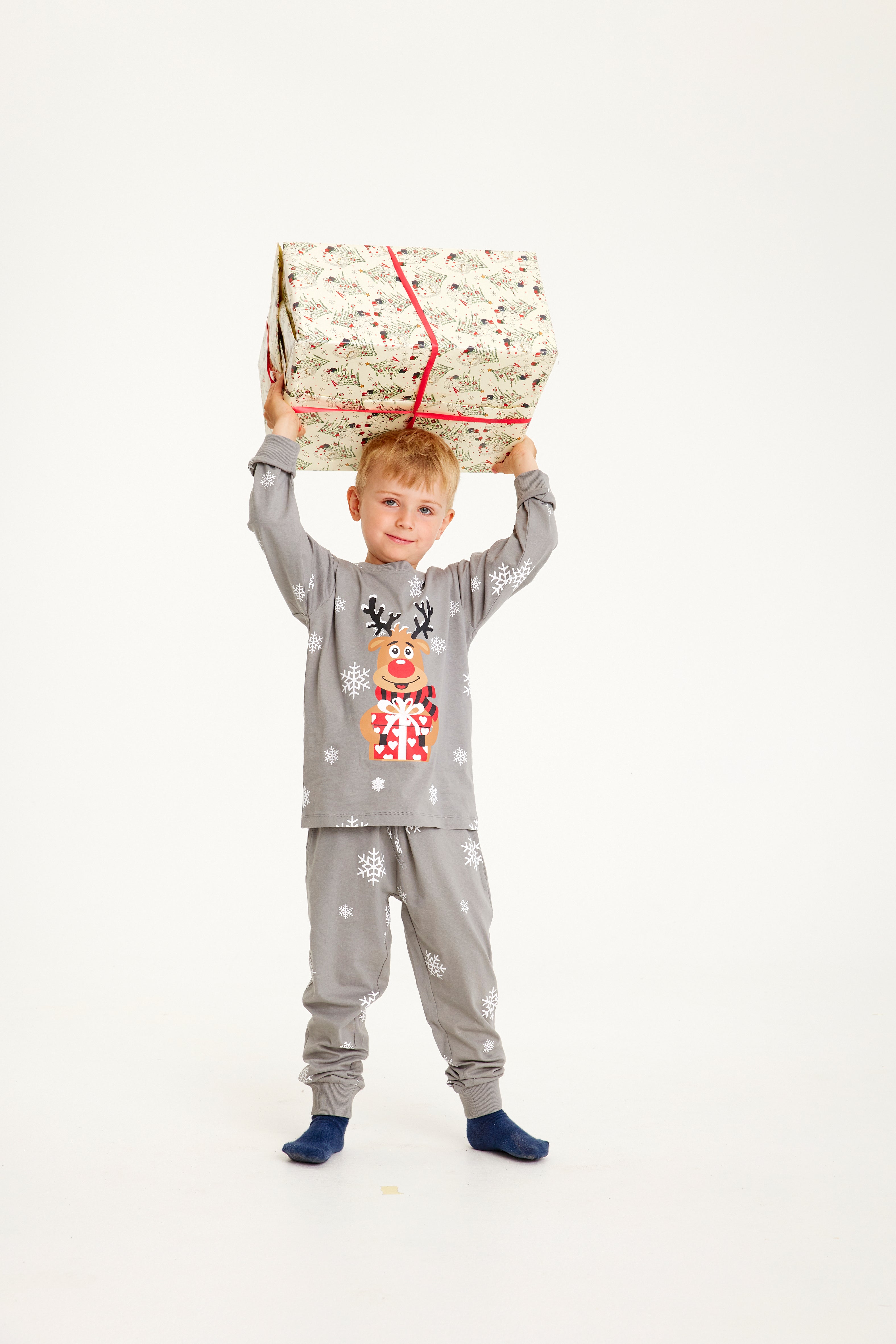 Et barn med en gave over hovedet er iført en grå julepyjamas.